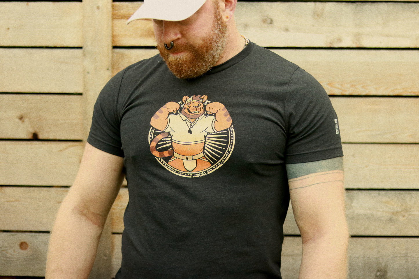 ginger wearing white hat covering eyes, and also wearing black heather t-shirt featuring a flexing tiger coach illustration from Bolt-wear.