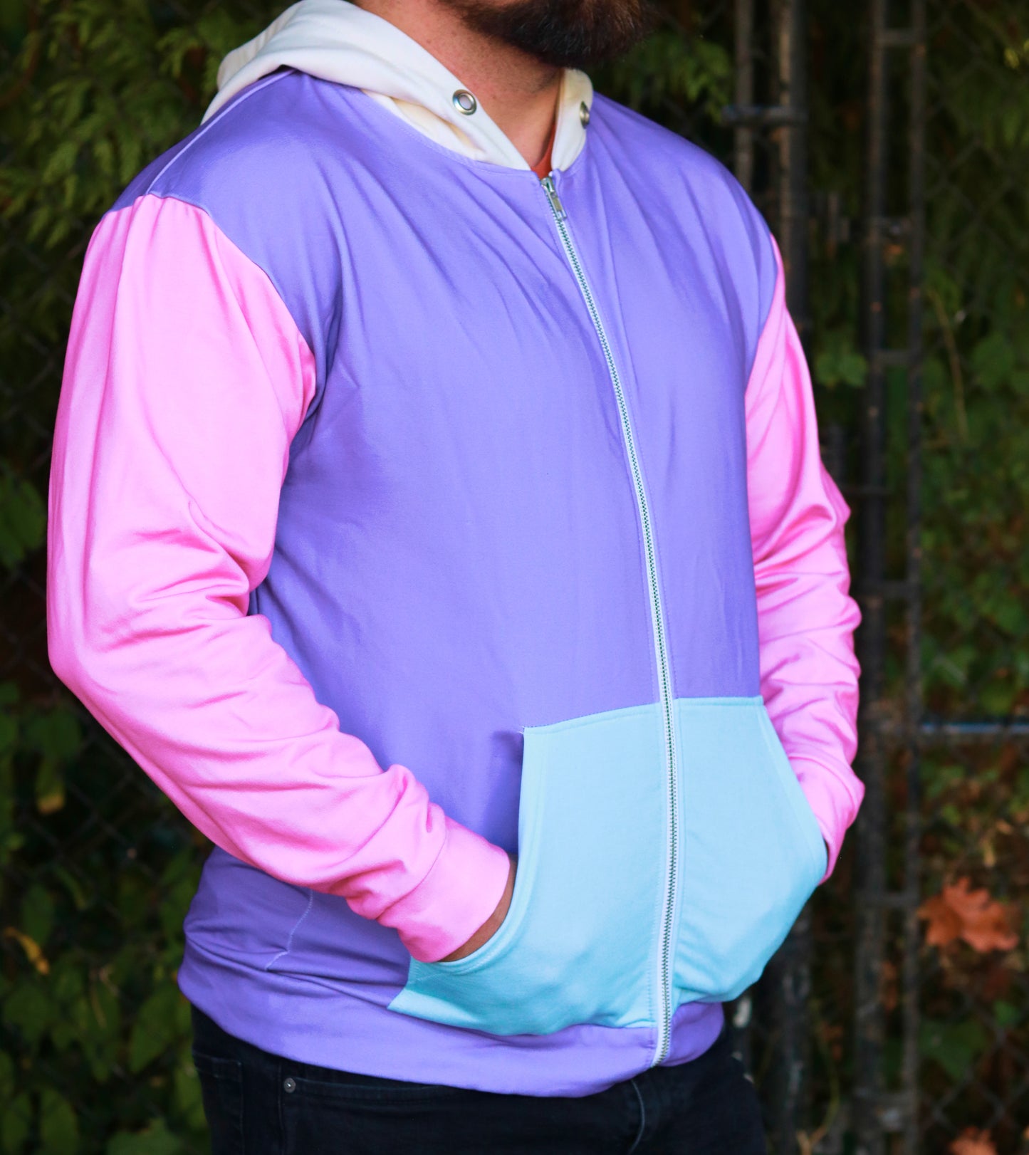 Person wearing a colorful jacket with pink sleeves and a blue pocket against a natural background.
