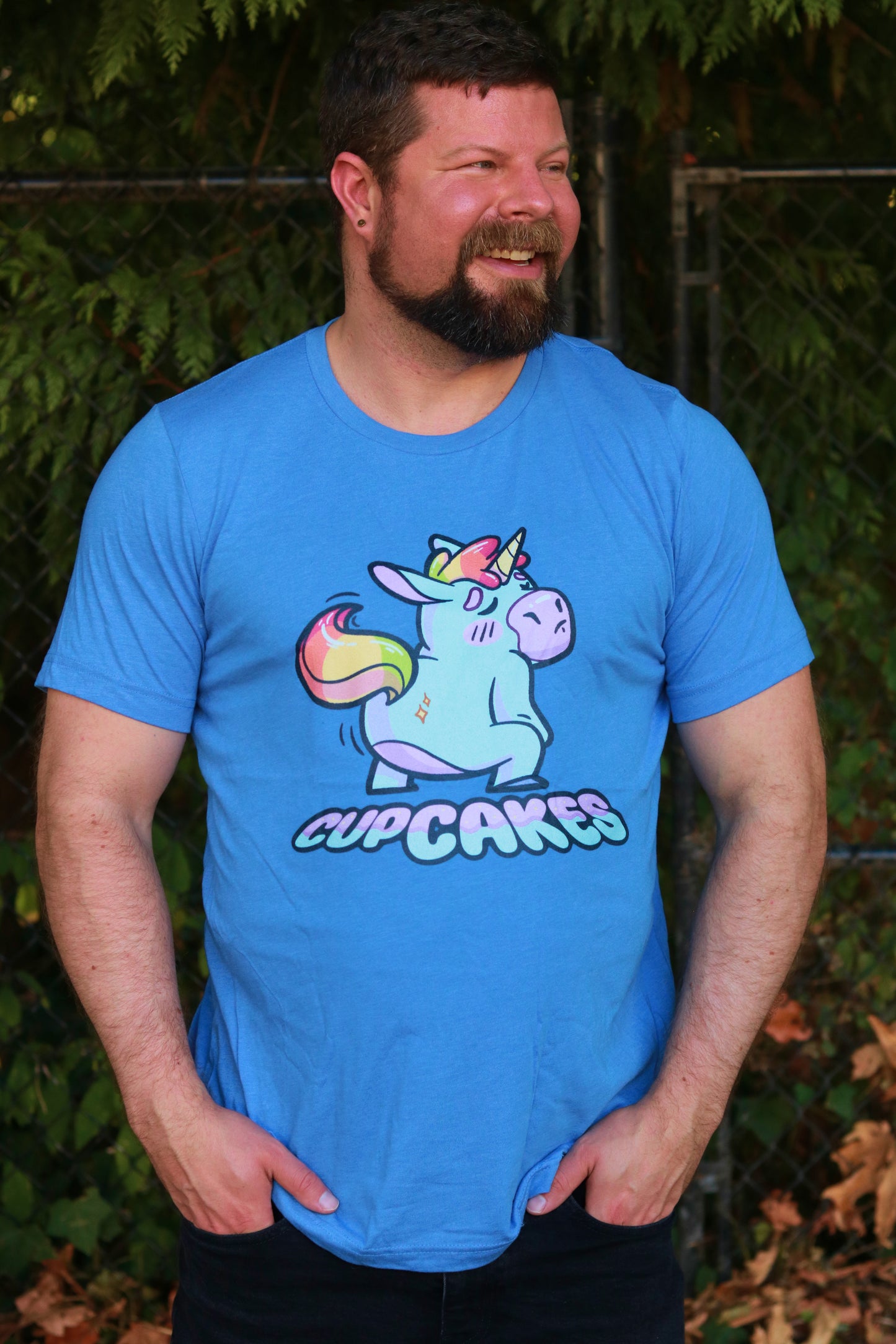 Man wearing a blue t-shirt with a colorful unicorn graphic and 'Cupcakes' text, standing outdoors.