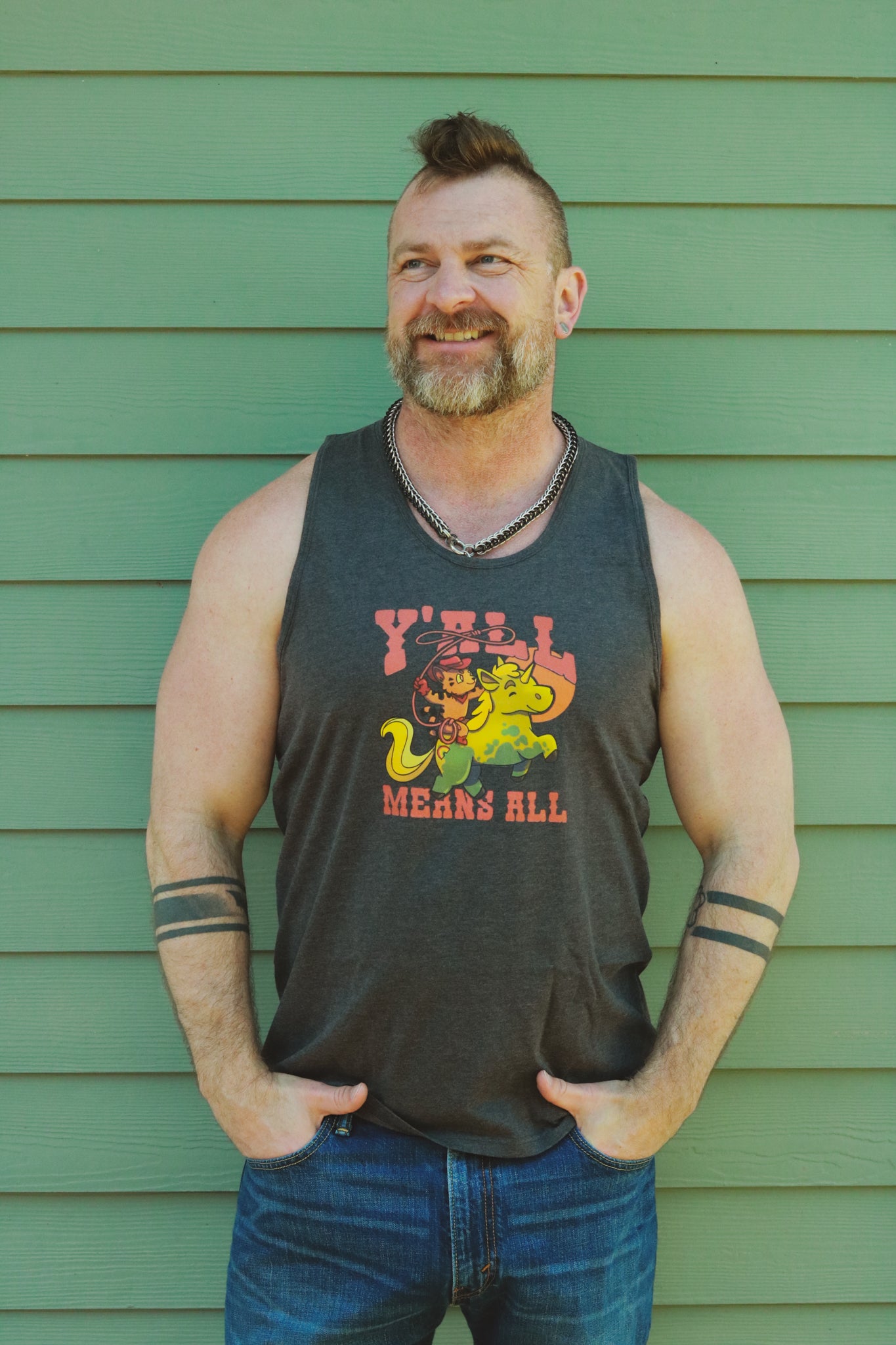 dark grey heather tank top worn by bearded daddy with mohawk in front of green wall, displaying tiger riding unicorn in rainbow colors and the text "y'll means all"