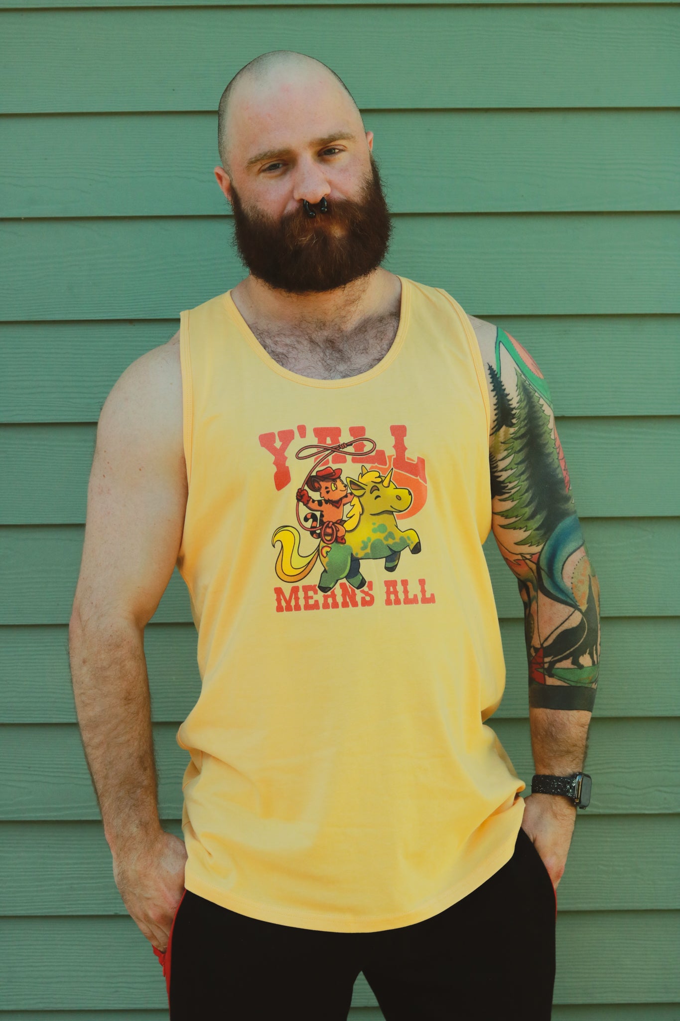 yellow tank top worn by bearded tattooed muscle pup, displaying tiger riding unicorn in rainbow colors and the text "y'll means all"