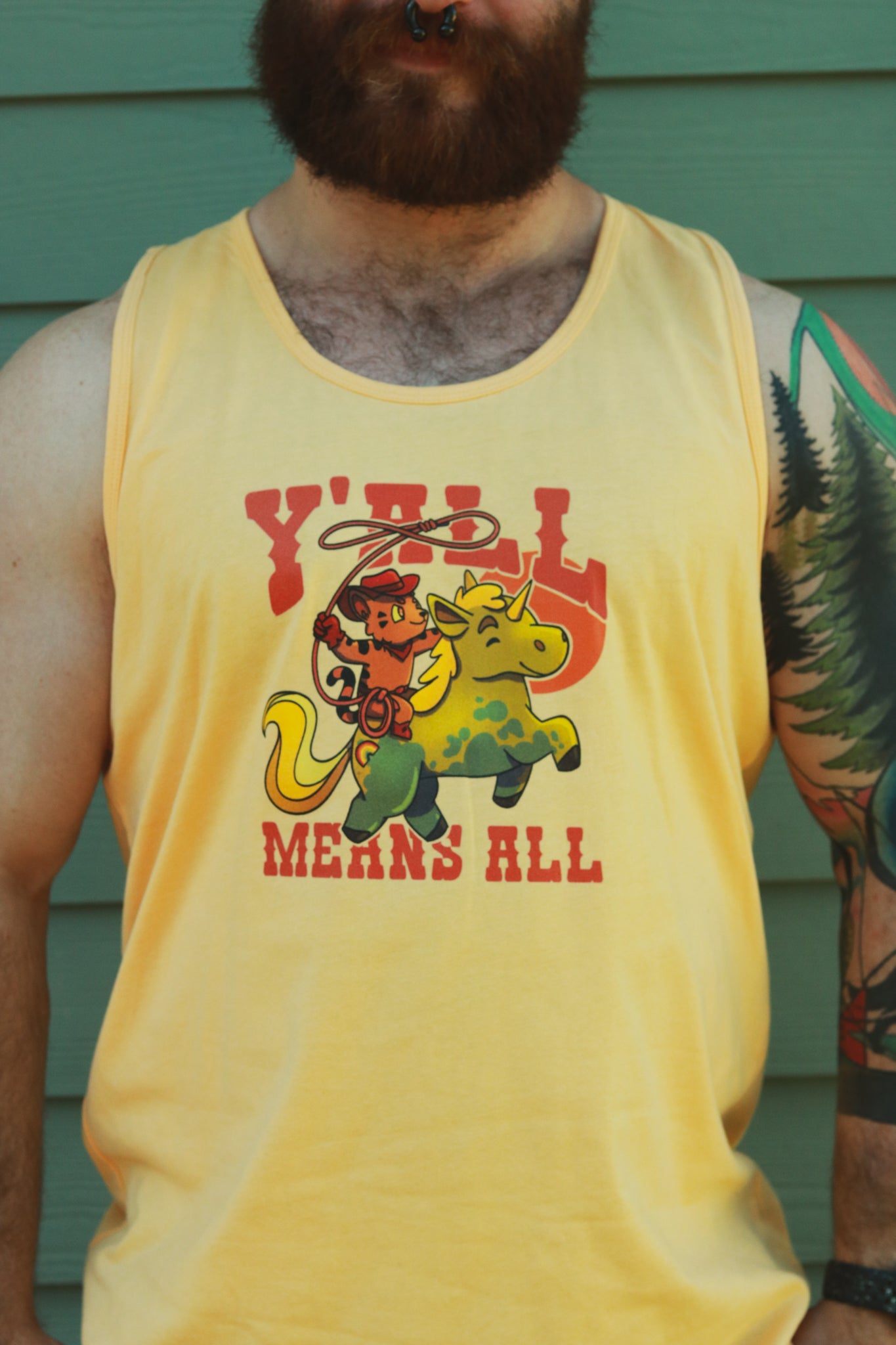 Yellow tank top worn by bearded ginger, displaying tiger riding unicorn in rainbow colors and the text "y'll means all"