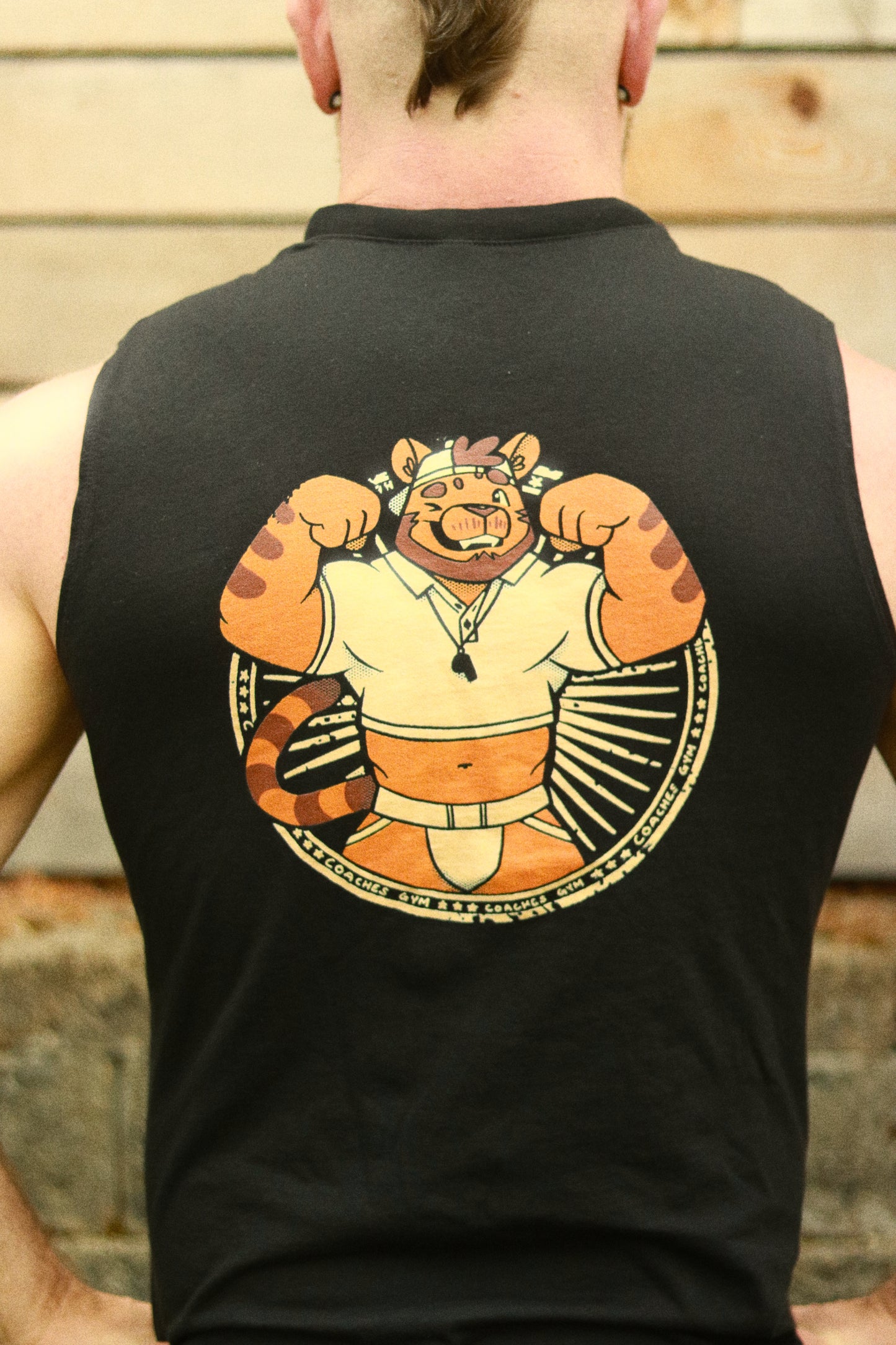 close up of flexing tiger coach design on black tank top, worn by man with mohawk