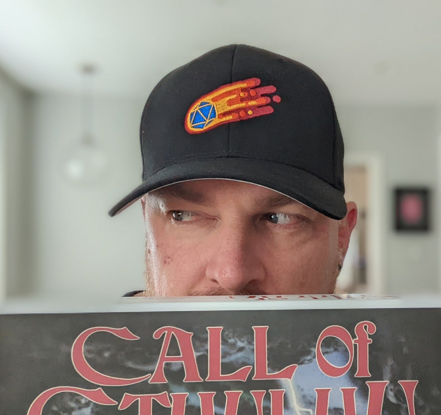 Grey D20 flaming comet baseball hat worn by man looking left over call of cthulu RPG