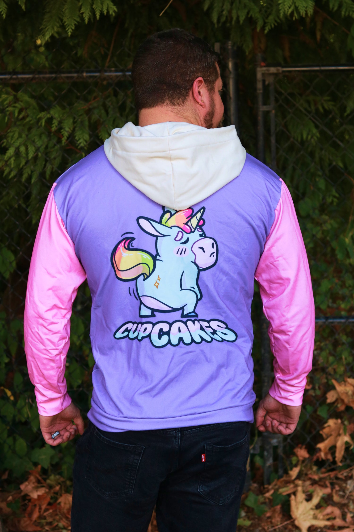 Person wearing a purple and pink jacket with a unicorn graphic and 'Cupcakes' text on the back, standing outdoors.