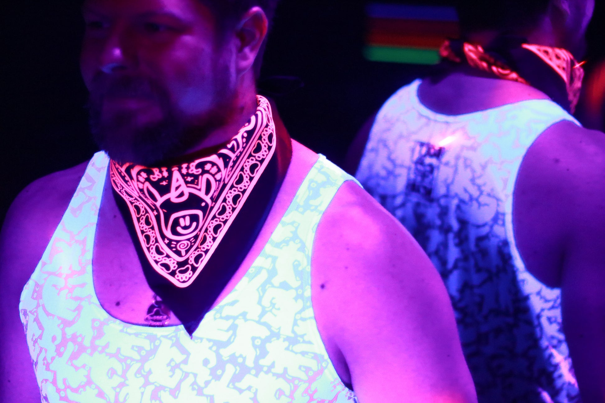 model in tank top wearing neon pink bandana featuring unicorn, lit by club lighting and black light.