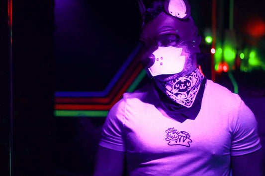 Man in leather dog hood wearing neon pink bandana lit by black light and club lighting, featuring tiger design.