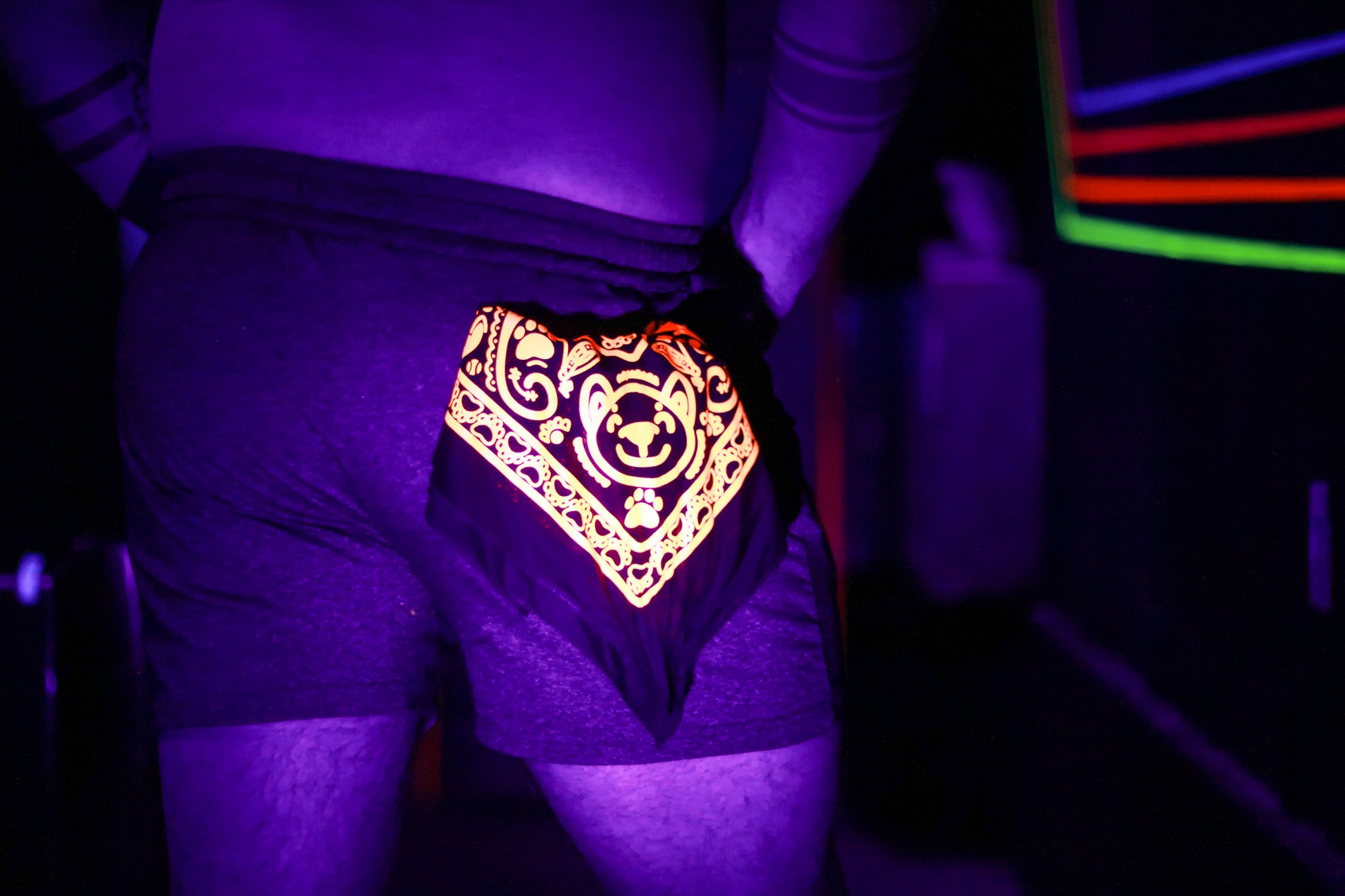 close up of neon orange colored bandana, in back pocket of model. lit by black light and club lighting