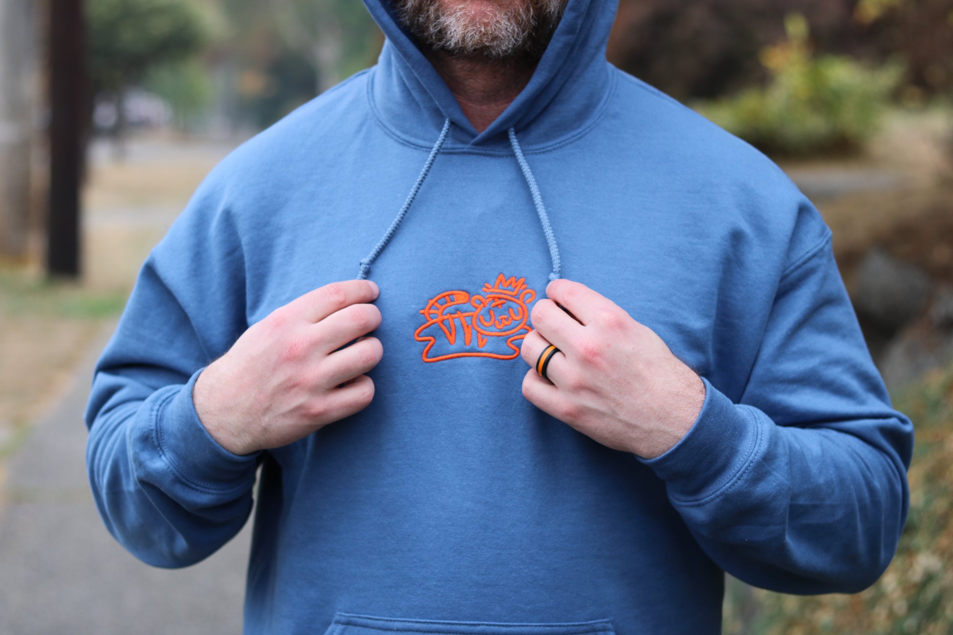 man with beard wearing royal blue pullover hoodie with bolt-wear tiger logo playing with hoodie tassels 