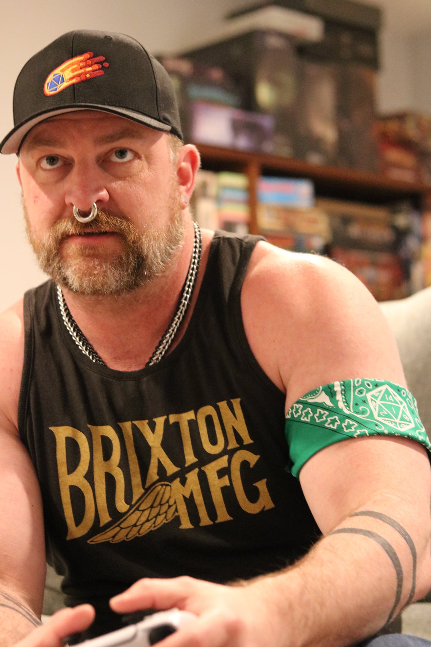 Brix, a handsome man with a beard and nose ring, wearing D20 comet themed hat, on his arm a green D20 dungeons and dragons themed bandana tied around.