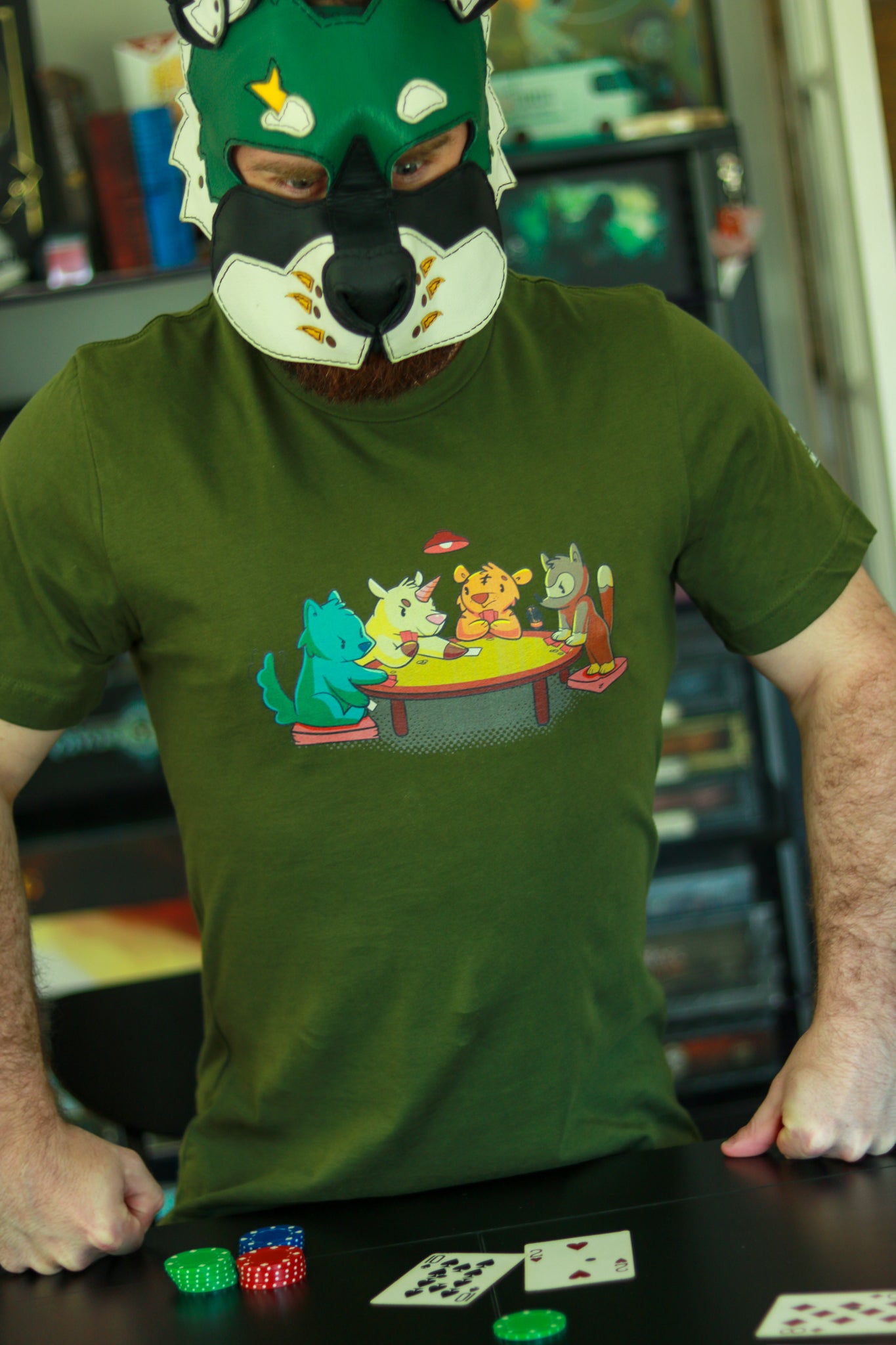 Dark Green t-shirt featuring 4 animals, a wolf, a unicorn, a tiger, and a racoon, playing cards around a table, worn by leather pup wearing green and white hood, playing cards.