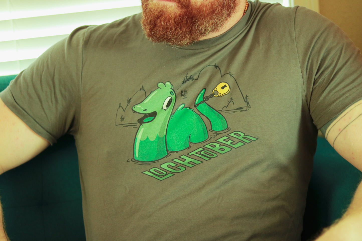 Grey Lochtober shirt featuring lochness monster with lock around tail, worn by bearded ginger.