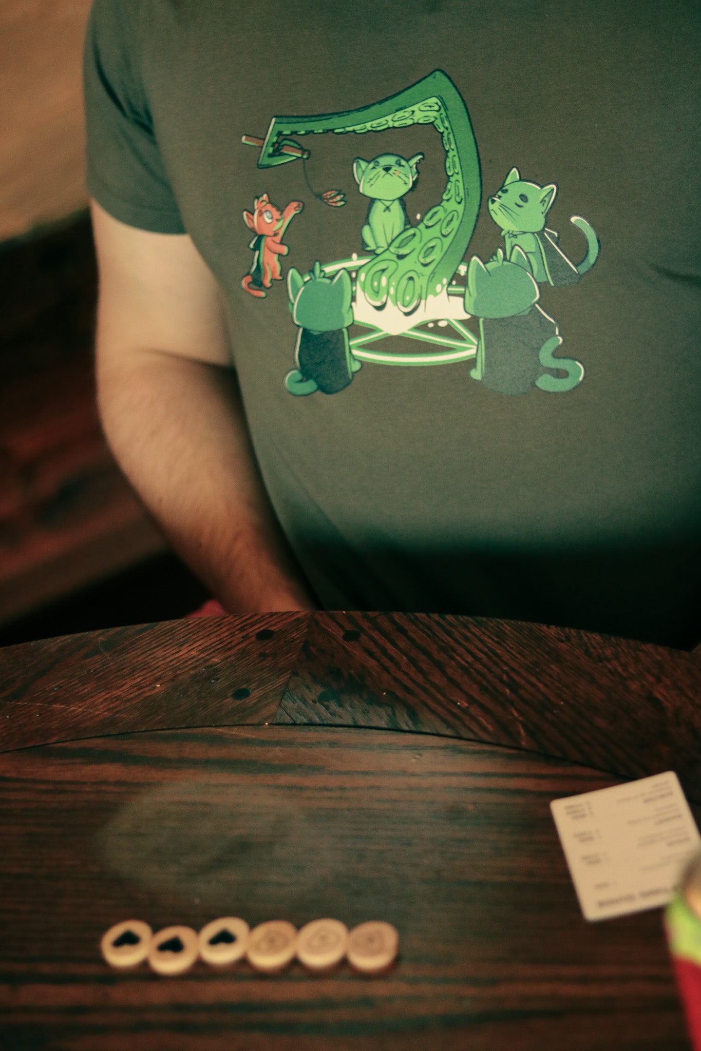 Person close up of chest wearing t-shirt featuring 5 cats summoning a tentacle, one an orange cat playing with a feather toy held by the tentacle
