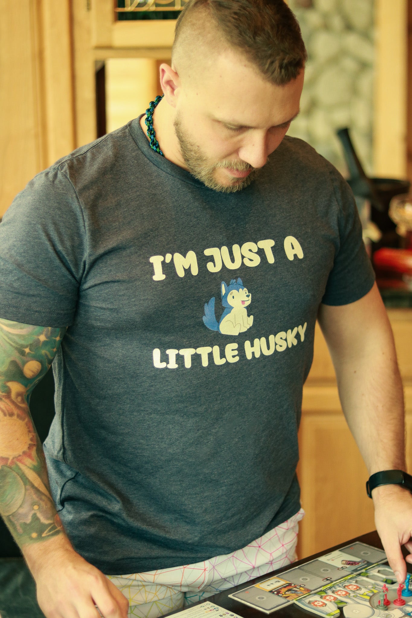 man with beard and tattoos playing boardgamesin wearing tshirt featuring image of small husky and text "I'm just a little husky"