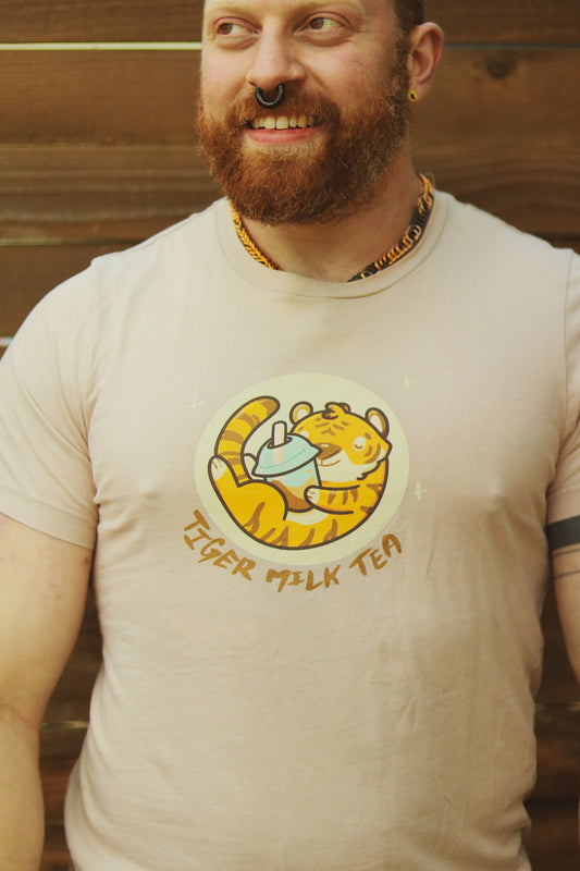 Bearded ginger with earrings and septum piercing standing in front of wooden wall wearing tan t-shirt featuring image of tiger holding bubble tea, with the words tiger milk tea underneath.