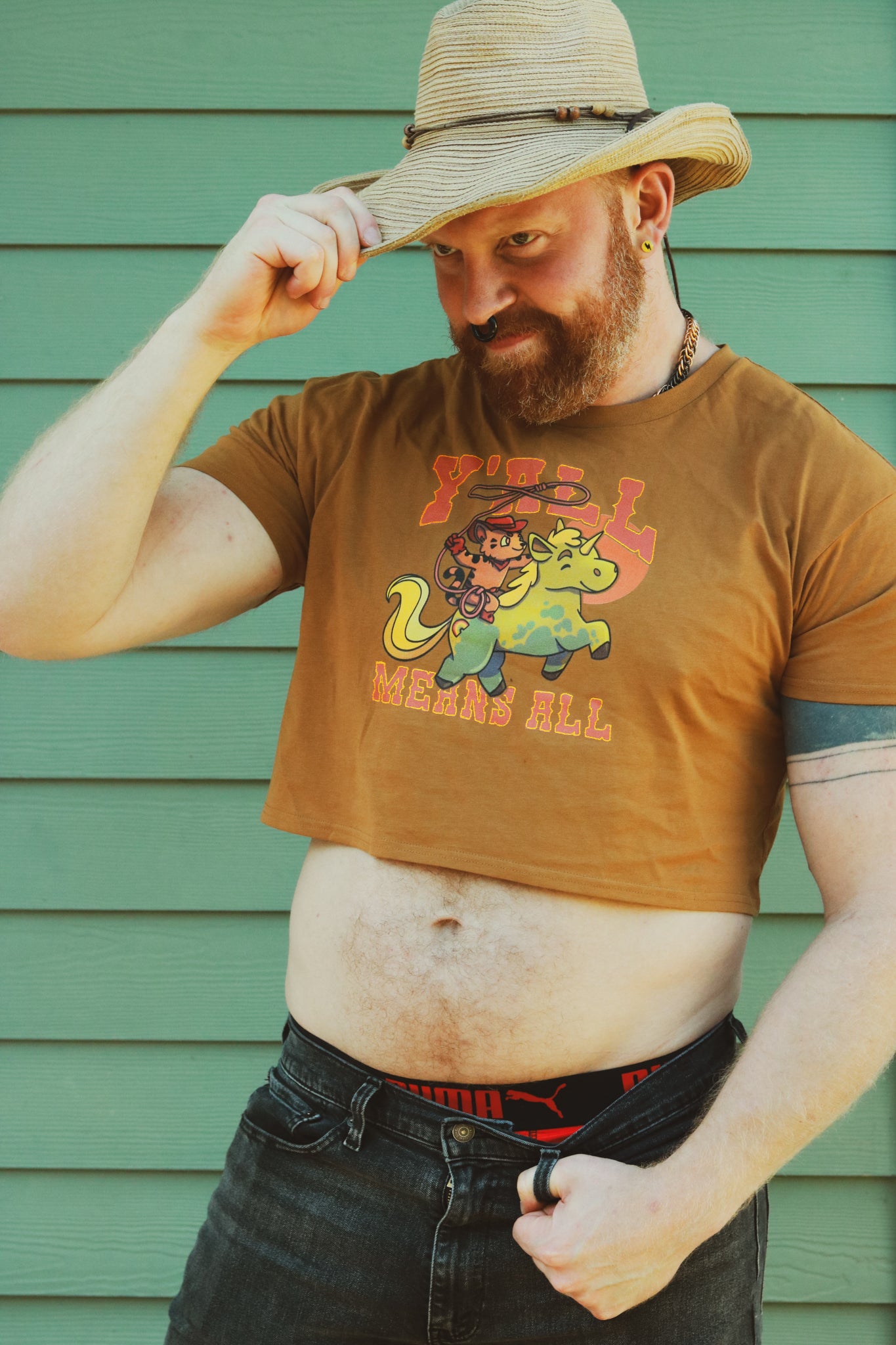 tan crop top worn by bearded ginger tipping a cowboy hat, displaying tiger riding unicorn in rainbow colors and the text "y'll means all"