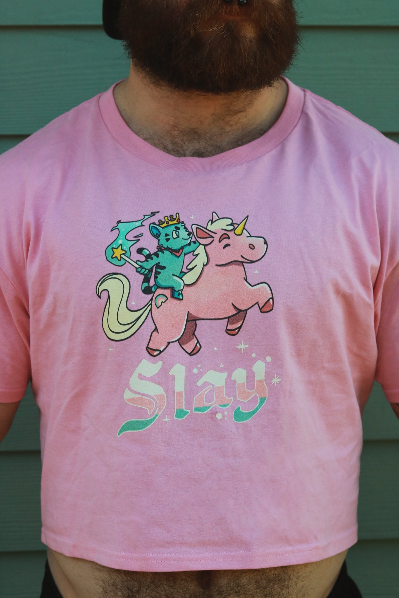 pink crop top with blue tiger riding pink unicorn, with the words slay below the image, worn by bearded hairy guy.