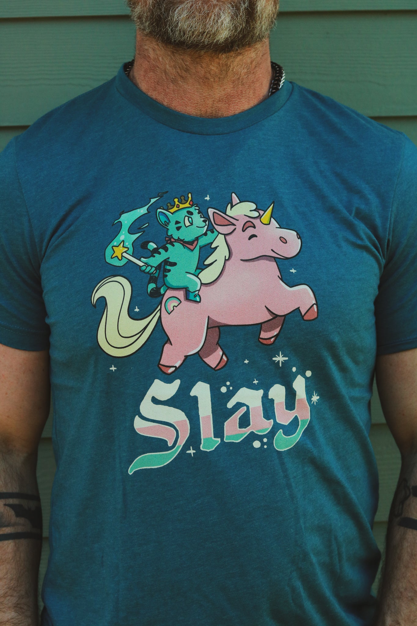 a blue heather tshirt with blue tiger riding pink unicorn, with the words slay below the image, worn by bearded hairy guy.